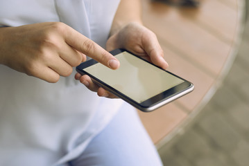 close-up of a girl holding a phone in dark color with a light screen on a background of a brown wooden table