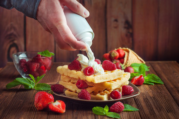 Males hand putting whipped cream on belgian waffle