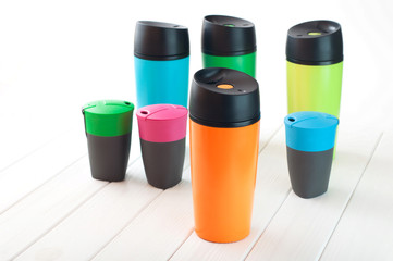 Many modern color thermos mugs on white wooden background