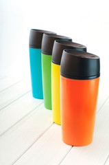 Series of color thermos mugs on the white wooden table