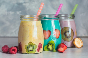 Three glass jars with fruit smoothie on the grey background