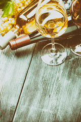 Бутылки с белым и красным вином, бокалы, виноград на деревянном столе
