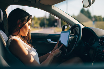 Attractive woman uses a digital tablet in a car on the road