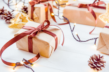 Christmas holidays composition with gifts in craft paper with satin ribbon on the white wooden background with copy space for your text. Selective focus