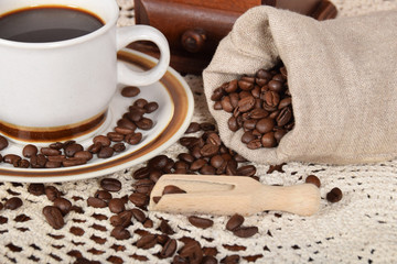 Grains of freshly ground coffee in a bag next to a cup of hot black coffee