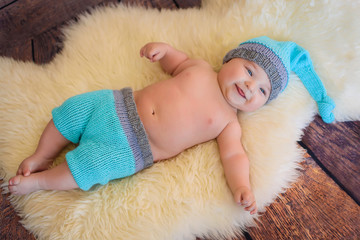 likable and pretty newborn baby boy with big blue eyes in a knitted hat on a wooden background at home