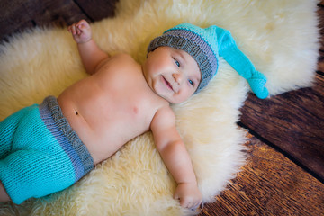 likable and pretty newborn baby boy with big blue eyes in a knitted hat on a wooden background at home