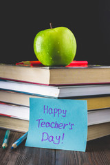 Concept of Teacher's Day. Objects on a chalkboard background. Books, green apple, plaque: Happy Teacher's Day, pencils and pens in a glass, sprig with autumn leaves.