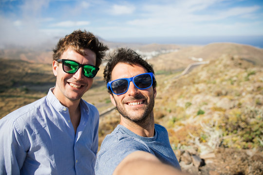 Two Smiling Men With Sunglasses Take Selfie Against Landscape