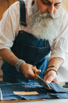 Indoor Portrait of Cool Senior Male Tailor Cutting Denim Fabric