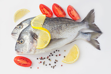 dorado raw raw uncooked with lemon and vegetables, tomatoes, onion, spices on a white background.