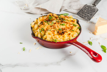Mac and cheese, american style macaroni pasta with cheesy sauce and crunchy breadcrumbs topping, in portioned pan, white marble table, copy space