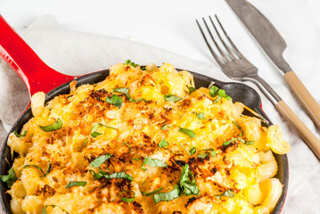 Mac and cheese, american style macaroni pasta with cheesy sauce and crunchy breadcrumbs topping, in portioned pan, white marble table, copy space