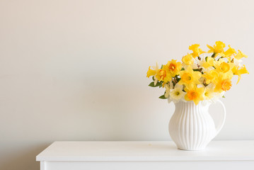 Jonquilles jaunes variées dans un pot blanc sur une table contre un fond de mur neutre