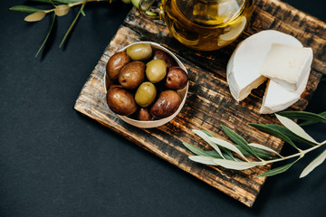 Dark and green olives, oil, goat cheese on a wooden board, top view, space for text