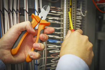 Cutters and screwdriver in hands of electrician close-up against background of electrical terminal block.