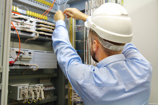 Electrician engineer at work inspecting cabling connection in industrial automation control fuseboard.