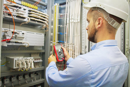 Engineer electric with multimeter. Side view of male technician examining fusebox with multimeter probe.