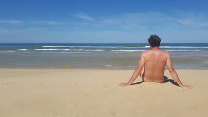 Fototapeta na wymiar naked man sitting on an empty beach and meditating