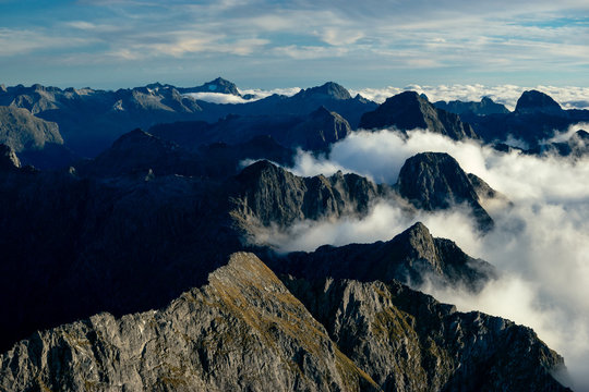 Sharp mountain peaks raising above the clouds in the south of new zealand in epic fashion.