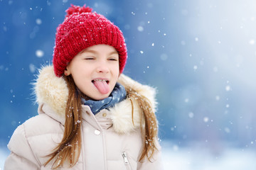 Adorable little girl catching snowflakes with her tongue in beautiful winter park. Cute child playing in a snow.
