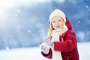 Adorable little girl having fun in beautiful winter park. Cute child playing in a snow.