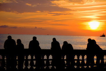 Fototapeta na wymiar silhouette of people leaning on railing at sunset facing the sea with a submarine sailing