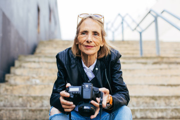 Senior woman holding her camera sitting on stairs.