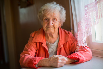 Elderly woman in red jacket sitting at table portrait.