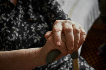 Old woman sitting with her hands on a cane