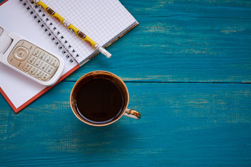 Coffee cup, smartphone and blank notepad on wooden table background.
