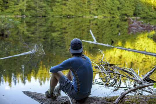 A man wearing a hat sits on a log next to Cedar Lake in Bellingham, Washington