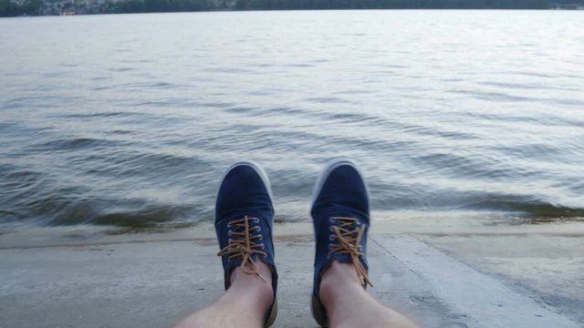 Point Of View: man sitting on a concrete jetty playing footsie, Relaxed time by the lake on a pier. POV