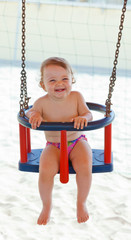 Joyful baby girl plays with the swing