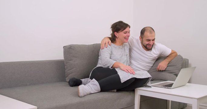 Couple at home sofa watching laptop and smiling 4k video. Happy man and woman using computer together, looking funny joke