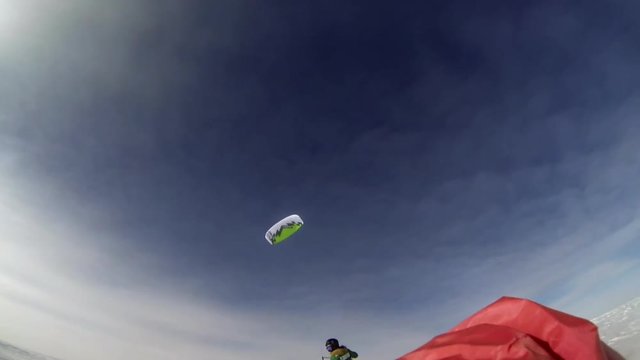 Shot of a man wearing a thick green jacket while parasailing his cute green and white colored parasail.