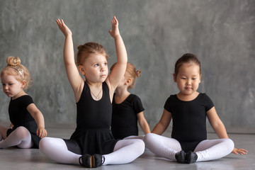 young woman ballerina in a black dress, white pantyhose and pointe shoes help stretch before the dance a small inattentive girl in a black dress to dance ballet well, in a dark dance studio