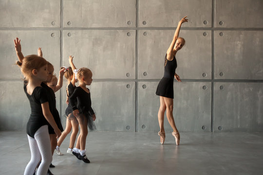 A young ballerina teaches to dance ballet of young girls ballerinas with black dresses, white pantyhose and pointe shoes in a dark dance studio