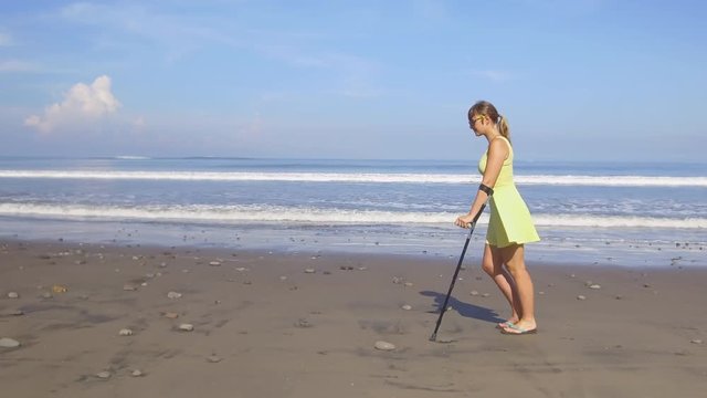 CLOSE UP: Strong woman in yellow dress walking with crutches along sandy ocean beach on summer vacation. Disabled girl on holidays strolling along the seashore. Traveling problems. Health insurance 