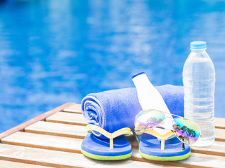 flip flops, sunglasses, blue towel and sunscreen at the side of swimming pool. Vacation, beach, summer travel concept