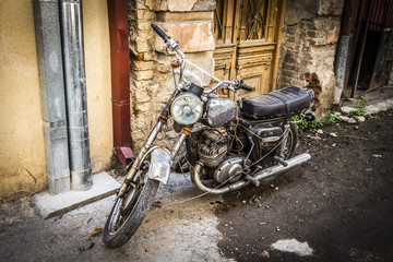 An old motorcycle stands near the entrance of the old house.