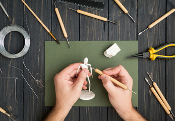 Craftsman hands working on human sculpture, sculpturing from polymer clay against working table...