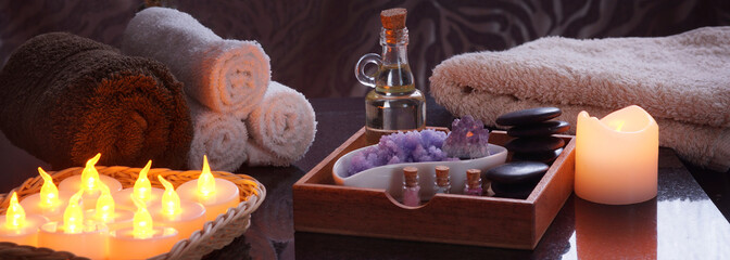 Set for spa treatments with electric burning candles and terry towels. In a wooden box oil and stones for massage, purple salt and amethyst, a set of multi-colored salt in jars.