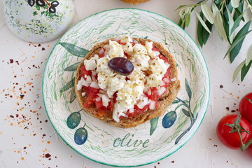 Dakos traditional greek appetizer on a traditional plate with ceramic olive oil jar, dry rye bread, olives and olive branch. Healthy eating concept. Mediterranian lifestyle