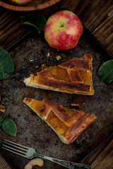 Sliced pieces of warm apple pie on rusty pan on wooden rustic table with fresh apples basket,...
