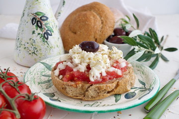 Dakos traditional greek appetizer on a traditional plate with ceramic olive oil jar, dry rye bread,...