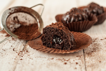 Chocolate chip muffin in brown wax paper. Unwrapped. Cocoa powder in the background