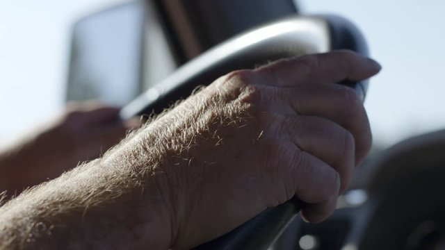 Detail of  truck driver's hands on wheel as he drives on a warm summer day. Interior, hand-held real time 4K