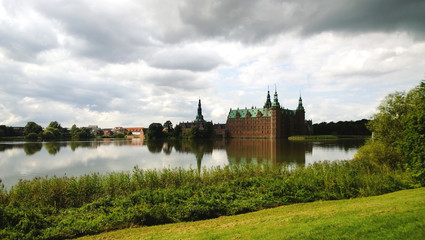 Obraz premium Zamek Frederiksborg na przedmieściach Kopenhagi Hillerød. W kadrze zamek, obok staw, na pierwszym planie piękny jasny trawnik