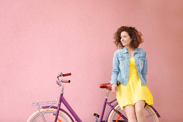 Beautiful young woman with bicycle on color background